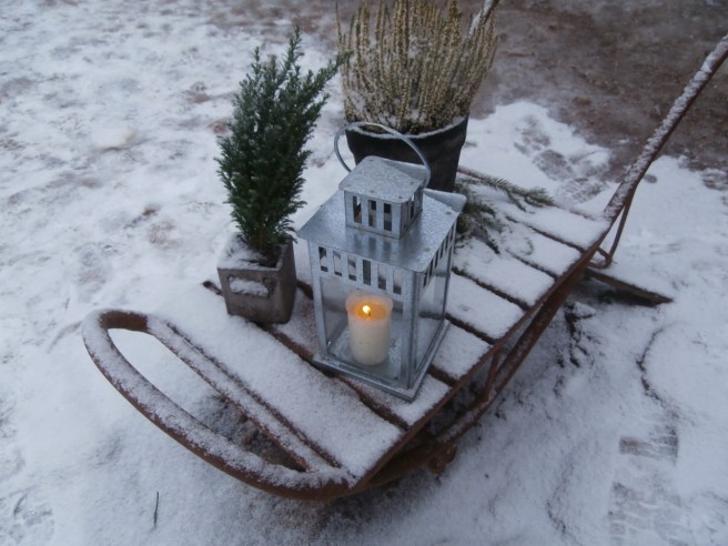 En kälke på gården är en fin prydnad med ljus i lykta och ett par växter.