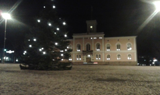 I väntan på bussen. En kur finns på torget. Det här är vårt rådhus och stadens julgran.