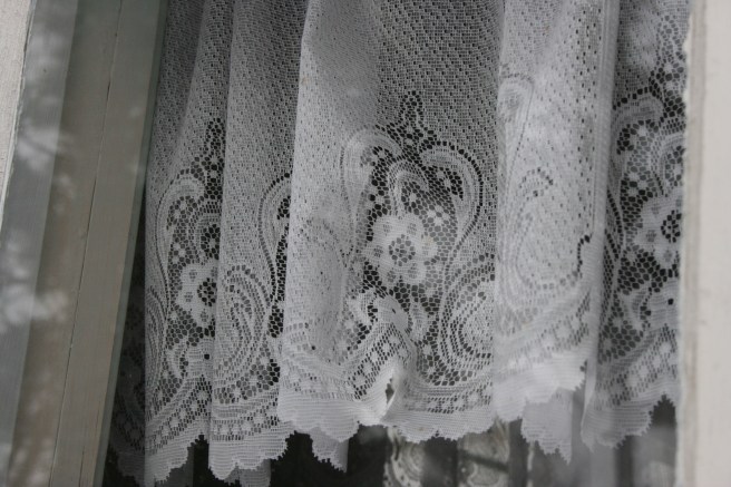 En vacker spetsgardin i fönstret till lilla verandan.